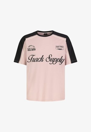 Rosa T-Shirt mit schwarzen Ärmeln, auf der Vorderseite mit schwarzem Text "Track Supply" und kleinerem Druck auf der oberen Brust "DAILY TRICK ROUTINES" und "CLUB LANE RIVAL MODE".