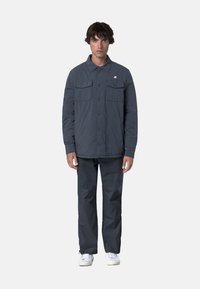 Giacca grigia con due tasche sul petto, chiusura a bottoni e maniche lunghe, abbinata a pantaloni grigi coordinati e sneakers bianche.