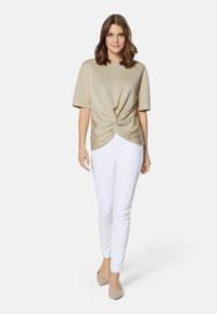 Beige korte mouwen top met een gedraaide voorkant, gecombineerd met witte slim-fit broek en beige hakken. Zacht materiaal, relaxte pasvorm.