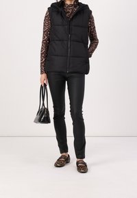 Svart vadderad väst med huva och dragkedja, bärs över en långärmad topp med brun leopardtryck, tillsammans med svarta läderbyxor och leopardmönstrade ballerinas.