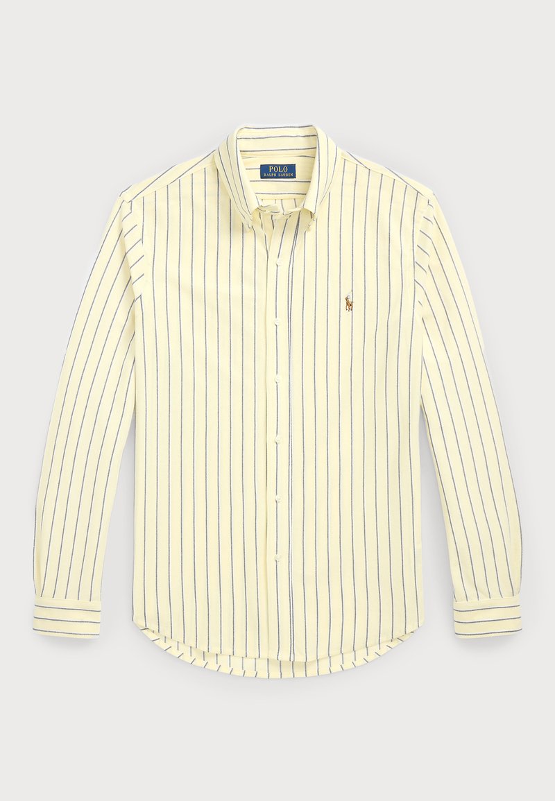 Srajca s gumbi v svetlo rumeni barvi z modrimi navpičnimi črtami. Ima ovratnik, dolge rokave, zaobljen rob in majhen logotip blizu prsi.