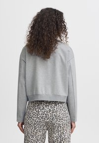 Sweatshirt court gris clair avec une coupe décontractée, des poignets côtelés et une texture lisse, associé à un pantalon à imprimé léopard. Aucun détail visible à l'avant.