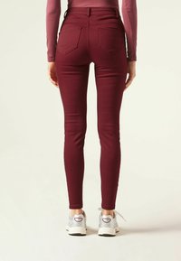 Jeans ajustados burdeos de cintura alta, con dos bolsillos traseros y una tela elástica y suave. Combinados con zapatillas blancas y plateadas.