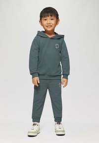 een aqua kleurige hoodie en bijpassende joggingsbroek, beide van zachte stof met een losse pasvorm. De hoodie heeft een voorvak en geborduurde details.
