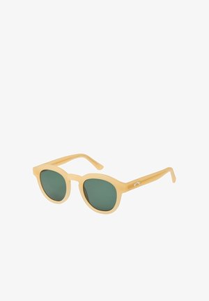 Beige zonnebril met ronde montuur, donkere groene glazen en iets dikke pootjes, geplaatst op een witte achtergrond.