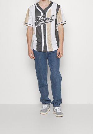 Baseball-style shirt in white, gray, and beige with vertical stripes, short sleeves, and a black logo. Paired with blue denim jeans and gray sneakers.