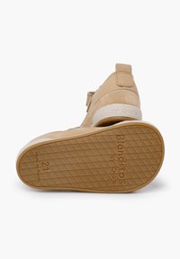 Scarpa in suede beige con suola in gomma bianca, caratterizzata da un motivo testurizzato sul fondo e un marchio sul lato e sul tallone.