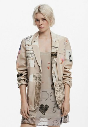 Beige blazer s různými tištěnými vzory, včetně textu, ilustrací a abstraktních designů. Hladká textura, jednoradový styl s ohrnutými rukávy.