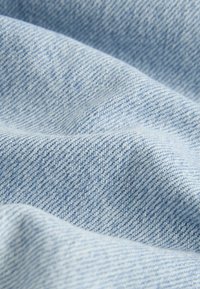 Tissu denim bleu clair avec un tissage diagonal visible et des plis doux créant des ombres délicates.