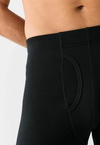 Leggings neri in cotone a costine con una vita aderente e dettaglio di apertura laterale, caratterizzati da una texture liscia e una vestibilità avvolgente in vita.