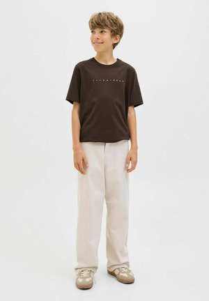 Dark brown cotton T-shirt with short sleeves and white printed text on the front, paired with light beige pants and light brown sneakers.