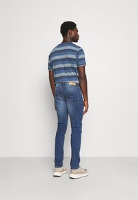 T-shirt a righe blu con maniche corte, abbinato a jeans slim-fit blu scuro. Dettagli notevoli includono un'etichetta color sabbia sulla cintura.
