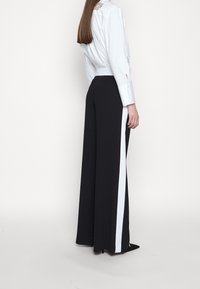 Svarta vida byxor med en vit sidrand. Tillverkade av ett slätt tyg, med en skräddarsydd passform och hög midja, bärs tillsammans med en vit skjorta.