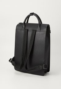 Mochila negra con material sintético suave, forma rectangular, dos correas de hombro de tela ajustables y un asa superior. Cierre con cremallera.