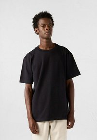 Schwarzes Baumwoll-T-Shirt mit kurzen Ärmeln und lockerer Passform. Verfügt über einen Rundhalsausschnitt und eine glatte Textur. Kombiniert mit hellen Hosen.