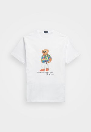 Witte T-shirt met korte mouwen met een afbeelding van een beer die een zonnebril draagt, een kleurrijk Hawaiiaans overhemd, witte broek en oranje schoenen.