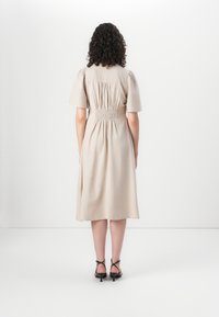Abito midi beige con maniche a sbuffo, dettagli arricciati in vita e una gonna fluida. Indossato con sandali neri con tacco.