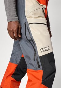 Hüdrosõltumatud püksid halli, oranži ja musta värviga. Omavad lukuga taskuid, logo plaastrit ning erinevaid tekstuure ja materjale.
