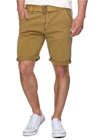 Szorty z khaki, z podwiniętymi nogawkami, paskiem i przednimi kieszeniami; do tego białe trampki z czerwonymi akcentami.