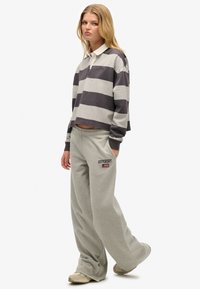Szara i ciemnoszara paskowana koszulka polo z długim rękawem, krótki fason z zapięciem na guziki, zestawiona z jasnoszarymi spodniami dresowymi z logo.