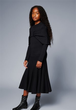 Black knitted long-sleeve top with a decorative bow and eyelet detail, paired with a matching flared skirt and black ankle boots.