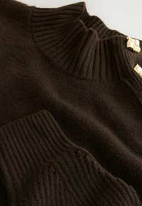 Hnědý pletený svetr s žebrovaným vysokým límcem, texturovaným tělem a zlatými akcenty v oblasti ramen. Měkký materiál a uvolněný střih.