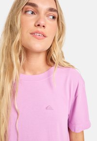 Λιλά βαμβακερό μπλουζάκι με στρογγυλή λαιμόκοψη, κοντά μανίκια και λεπτομέρεια με λογότυπο σε τόνο στο αριστερό στήθος. Λείο υλικό και άνετη εφαρμογή.