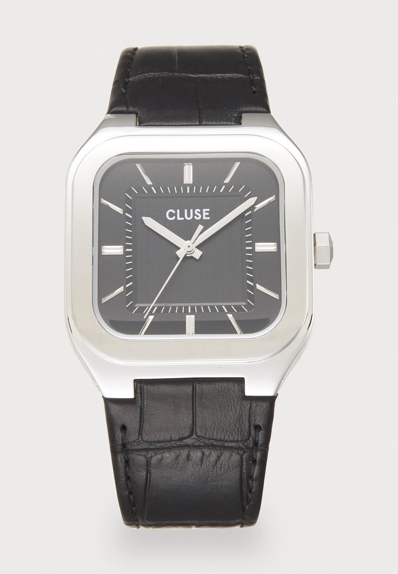 Montre rectangulaire argentée avec un bracelet en cuir noir texturé et un cadran gris foncé. Les caractéristiques incluent des index des heures blancs et des aiguilles argentées.