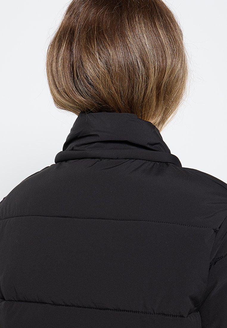 Doudoune noire avec un col haut, présentant des sections matelassées et une texture douce et lisse. L'arrière présente une finition soignée sans matériel visible.