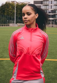 Erksu roosa tõmblukuga spordijope hallide aktsentidega ja kolme triibuga detailidega varrukatel. Sile tekstuur ja kindel disainielementidega.