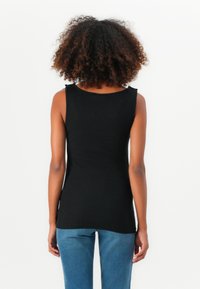 Top negro sin mangas de tela suave, con escote redondeado y corte ajustado. Combinado con jeans azules.
