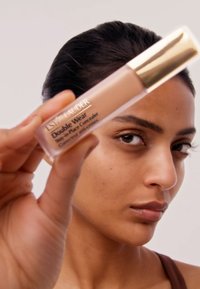 Estée Lauder Double Wear Stay-in-Place Concealer, ovan läskande i en klar tube med ett gyllene lock, innehållande ljusbrun vätska och svart text på etiketten.