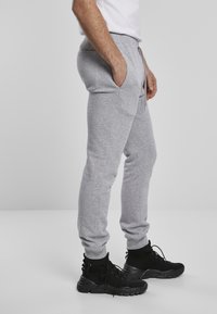 Grå sweatpants i mjukt tyg, med sidofickor, elastisk midja med snörning och tapered mudd. Bärs med svarta sportskor.