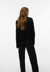 Juodas megztinis laisvo silueto su ilgomis rankovėmis, derinamas su juodomis kelnėmis. Audinys atrodo minkštas, lygios tekstūros, be matomų raštų.