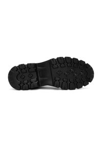 Suela de zapato de goma negra con surcos profundos y superficie texturizada, diseñada para ofrecer agarre y durabilidad en entornos al aire libre.
