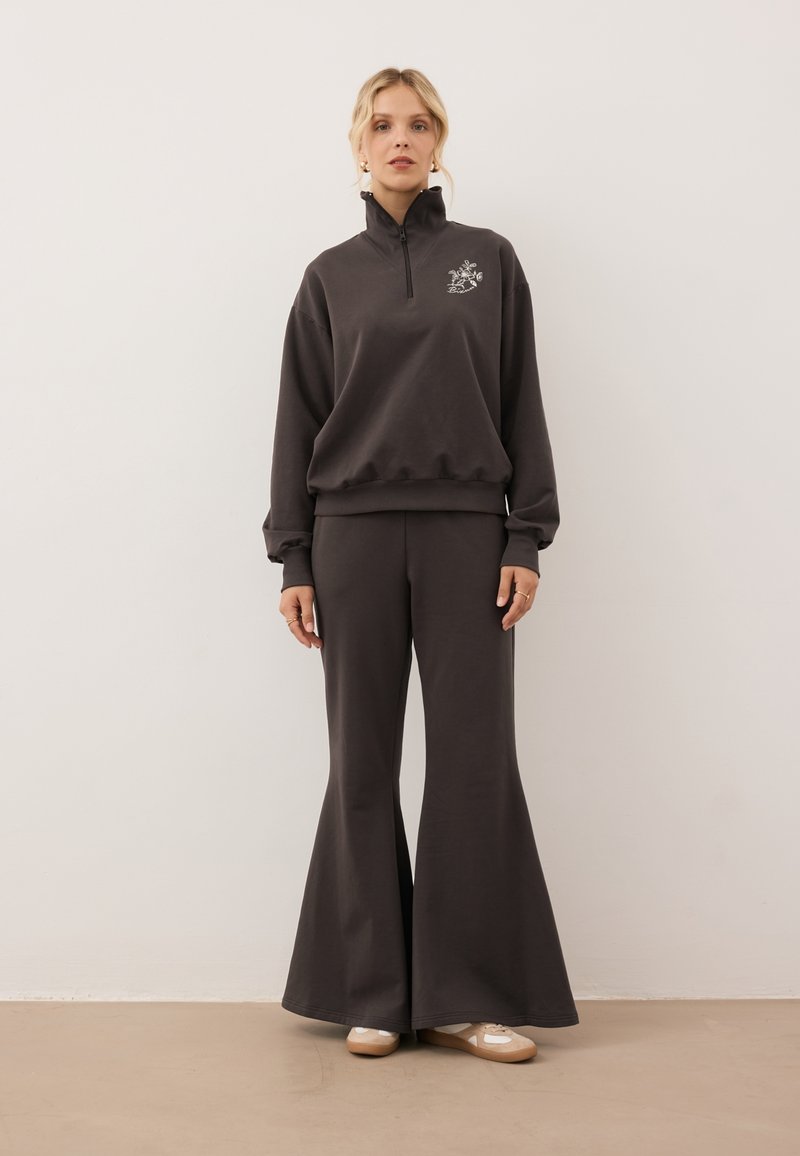Donkergrijs coördinaatoutfit met een ritssluiting sweatjack met bloemembroidery en flared broek. Zachte stof met een relaxed fit.
