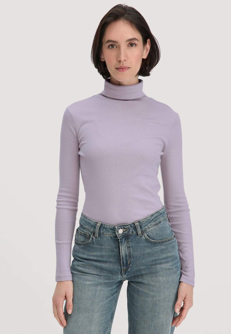 Hellvioletter Rollkragenpullover mit langen Ärmeln, aus elastischem Stoff. Kombiniert mit hochgeschnittenen blauen Jeans. Glatte Textur.