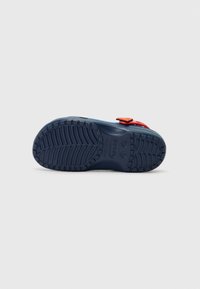 Blue rubber shoe sole with deep tread pattern. Features a red strap with a yellow emblem. Smooth texture with no additional patterns.