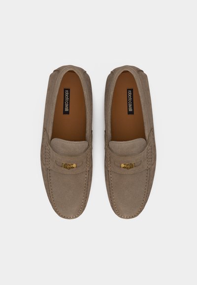 Paire de mocassins beige en daim avec détail en métal doré sur le dessus et étiquette de la marque visible à l'intérieur de chaque chaussure, vue de dessus.