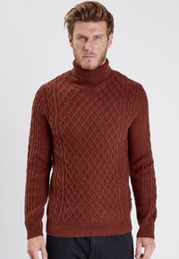 Pull en maille brun à col roulé présentant un motif en losanges texturé avec des accents en torsade. Manches longues et poignets et ourlet côtelés.