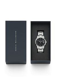 Montre en acier inoxydable avec un cadran noir et des accents argentés, présentée dans une boîte marine avec un intérieur noir. Elle possède un guichet de date et un bracelet élégant.