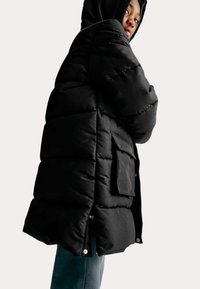 Zwarte pufferjack met een doorgestikt ontwerp, met capuchon, zijzakken en een licht cropped lengte, die een gladde textuur toont.