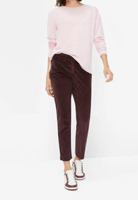 Tmavě burgundské kordové kalhoty se slim-fit střihem, spárované s dlouhým rukávem světle růžového topu a bílými teniskami s burgundskými akcenty.