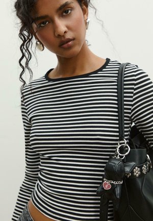Maglia a maniche lunghe bianca e nera a righe con scollatura rotonda. Borsa nera con hardware argentato e un accessorio portachiavi a forma di cane.