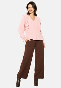 Light pink blouse with ruffles along the front, V-neckline, and button closure. Paired with brown wide-leg pants and brown ankle boots.