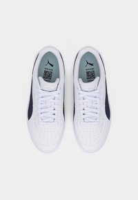 Ζεύγος λευκών και μαύρων αθλητικών παπουτσιών Puma με κορδόνια, σε άποψη από πάνω, που δείχνει τα εσωτερικά πέλματα με το λογότυπο Puma και κωδικούς QR.