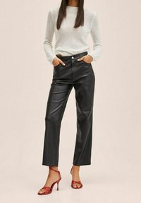 Pantalones de imitación de cuero negros de pierna ancha con cintura alta, con un cierre frontal de botón y sutilezas en las costuras, combinados con tacones rojos con tiras.