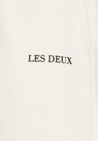 Sweat-shirt en coton blanc avec l'inscription "LES DEUX" en broderie noire. Le tissu présente une finition lisse et texturée.