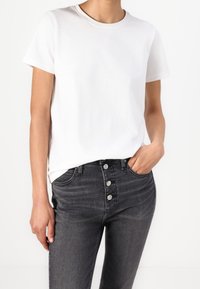 Vit bomull t-shirt med korta ärmar, rund halsringning, i kombination med mörkgrå jeans med hög midja som har femknapsstängning.