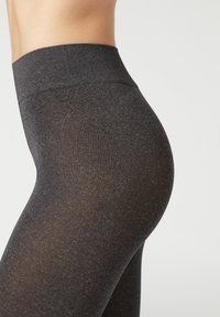 Hoch geschnittene schwarze Leggings aus einem dehnbaren, matten Stoff. Sie verfügen über eine glatte Textur und eine einfarbige Gestaltung ohne Muster oder Akzente.
